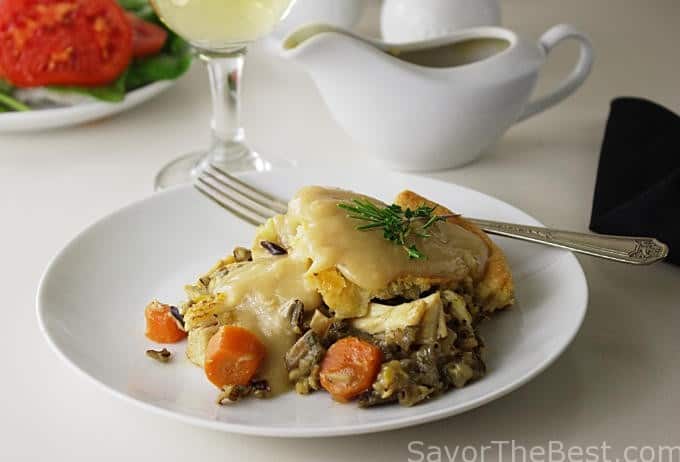 A slice of chicken pot pie next to a gravy boat. 