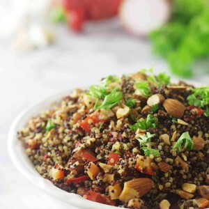 Quinoa pilaf in a serving bowl with vegetables in the background.