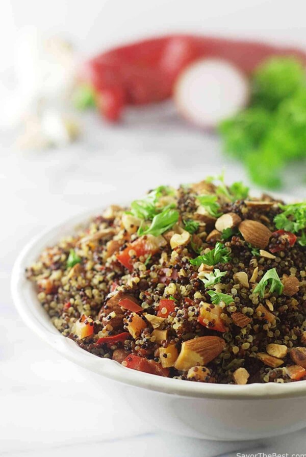 Quinoa pilaf in a serving bowl with vegetables in the background.