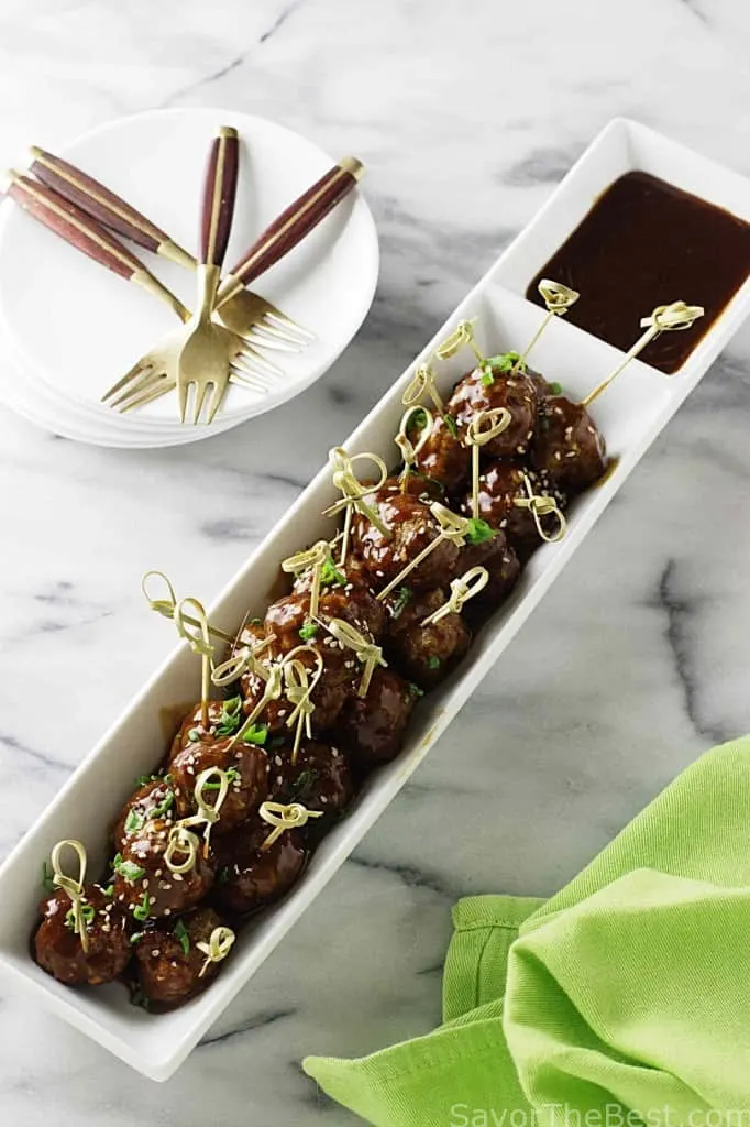 A serving dish of teriyaki meatballs and some appetizer forks. 