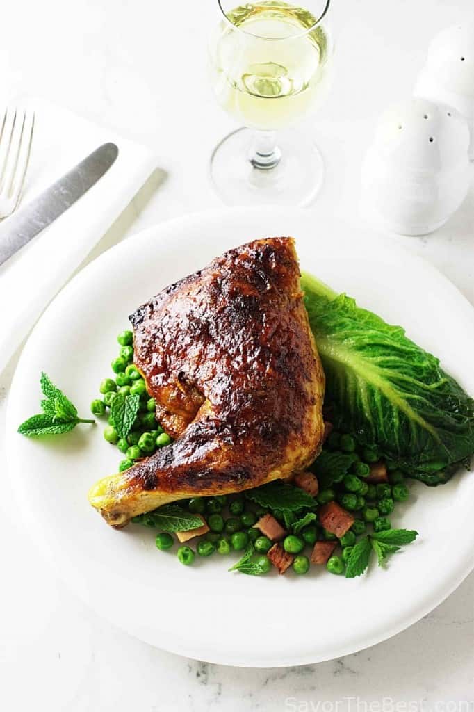 A roasted chicken quarter leg on a bed of peas and carrots.