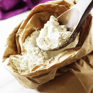 A wooden spoon scooping out some gluten free flour from a paper bag.