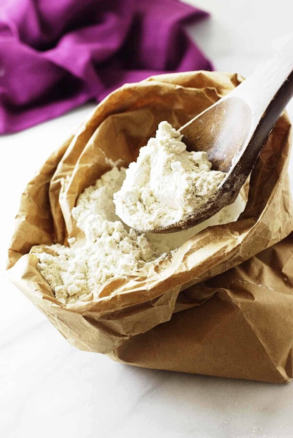 A wooden spoon scooping out some gluten free flour from a paper bag.