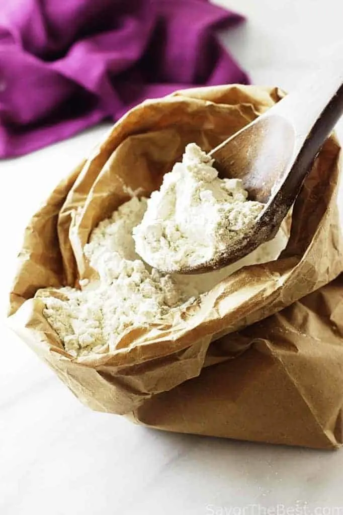 A wooden spoon scooping out some gluten free flour from a paper bag.