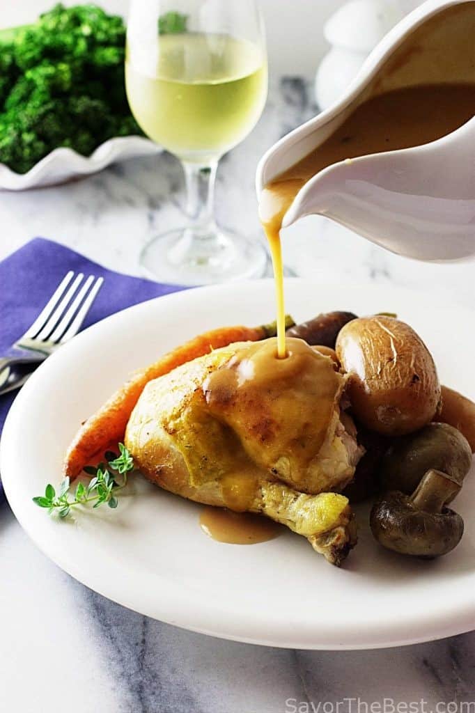 A serving of roasted chicken on a plate with potatoes, carrots and mushrooms. Drizzling gravy over the top. 
