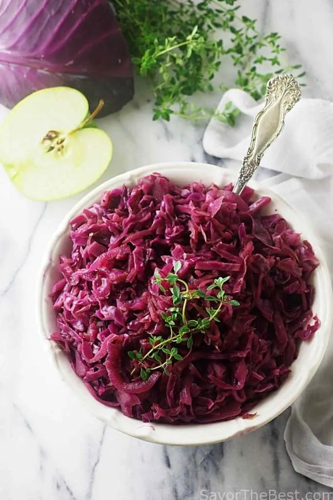 German red cabbage in a serving dish next to an apple. 