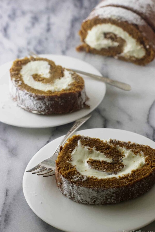 Two plates with slices of a pumpkin cake roll next to forks.