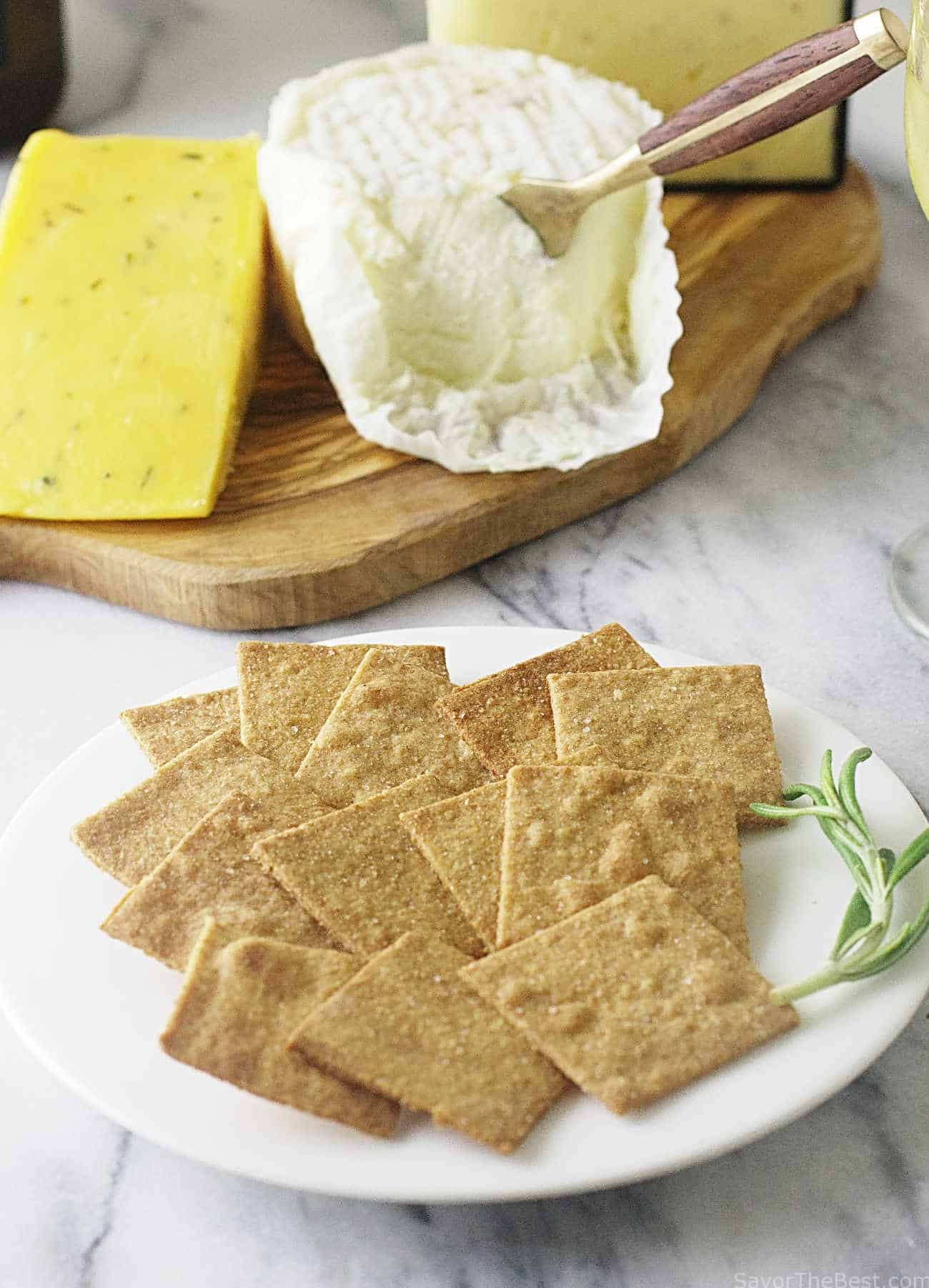 Einkorn wheat thin crackers on serving plate with cheese in the background.