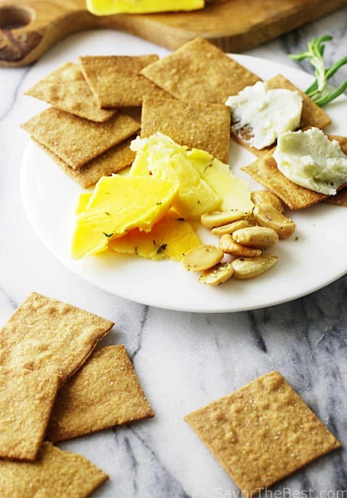 Crackers on a marble tray next to a plate with more appetizers. 