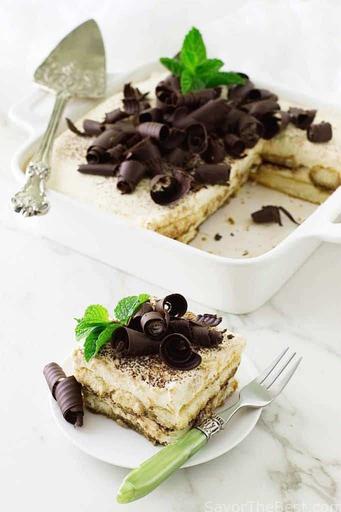 A slice of tiramisu in front of a dish with more dessert. 