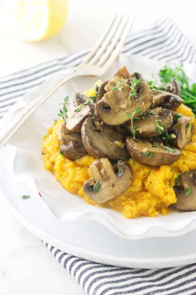 Herbed mushrooms over an orange squash mash. Green herb sprigs and a fork are around the dish.