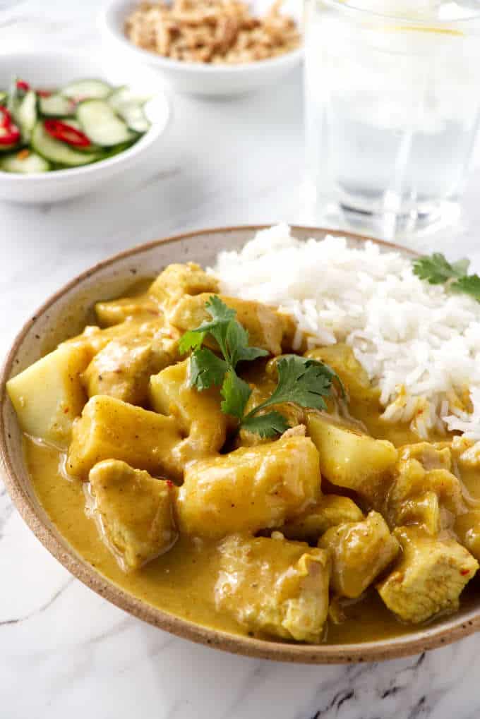 angle shot of Thai Yellow Curry Chicken and Potatoes with a glass of water and a salad