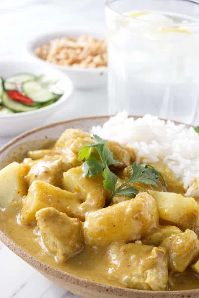 Close up of a bowl of Curry Chicken and Potatoes with salad in the background