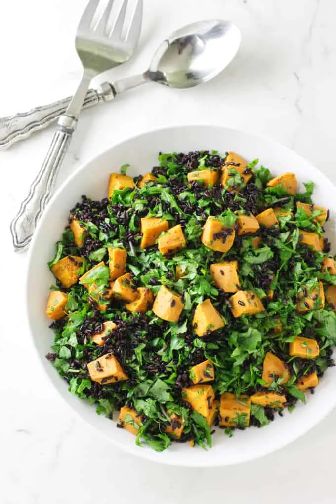 A serving bowl with with sweet potato and kale salad with black rice. 