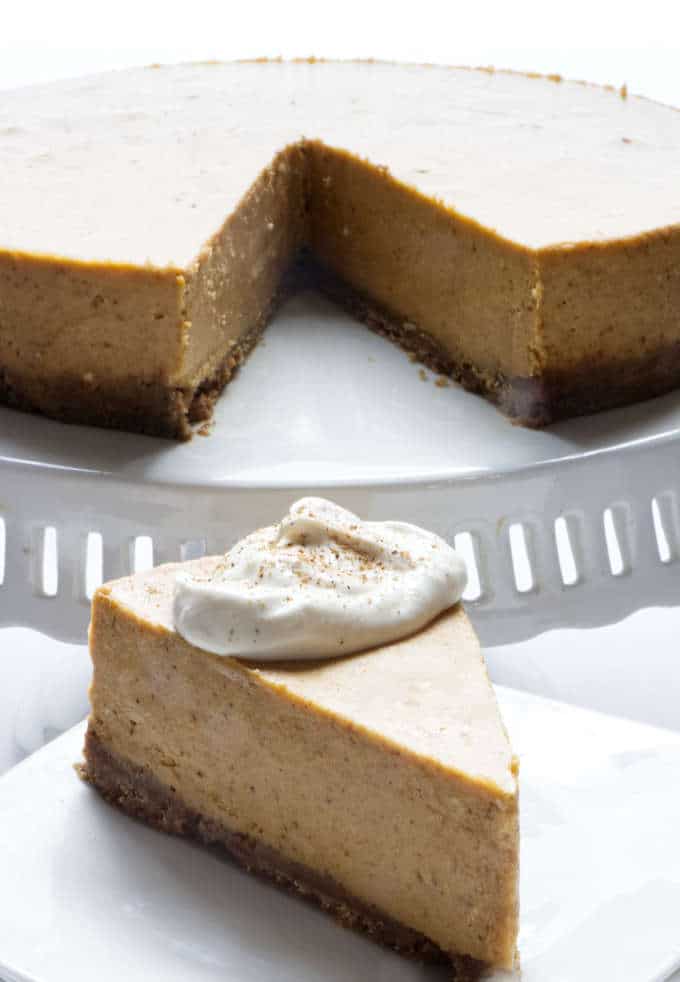 Spice pumpkin cheesecake on a cake stand with one slice removed and set on a small serving plate.