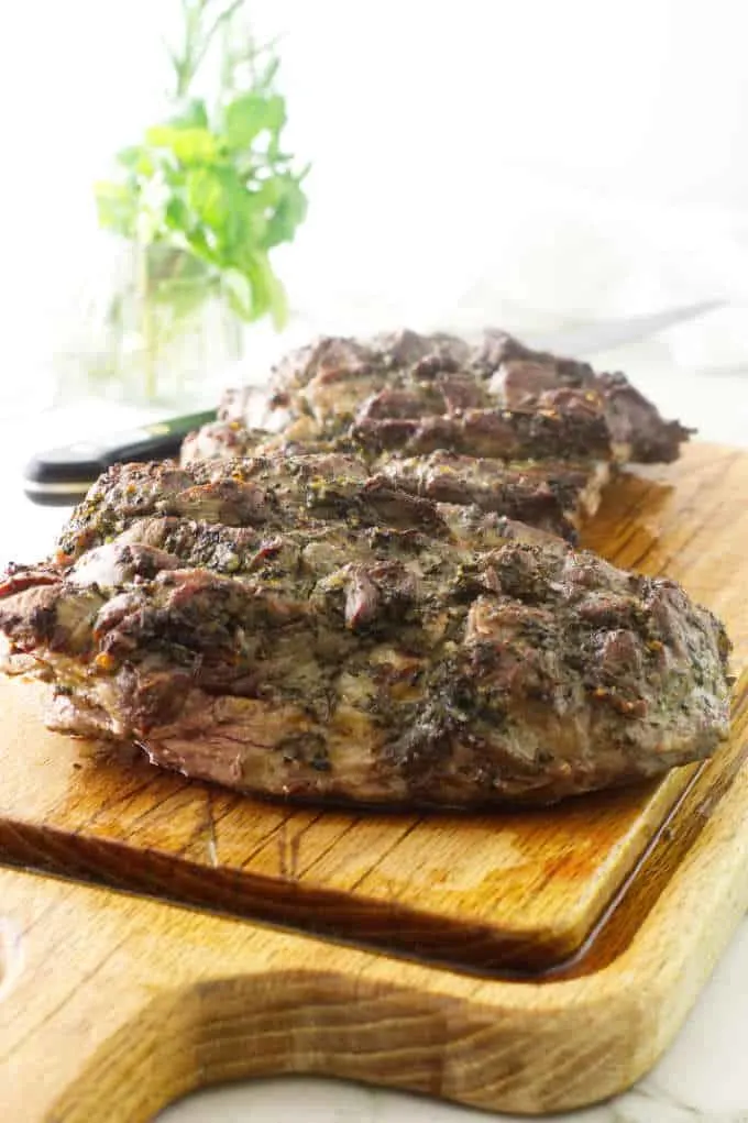 roasted lamb on a cutting board with herbs in the background