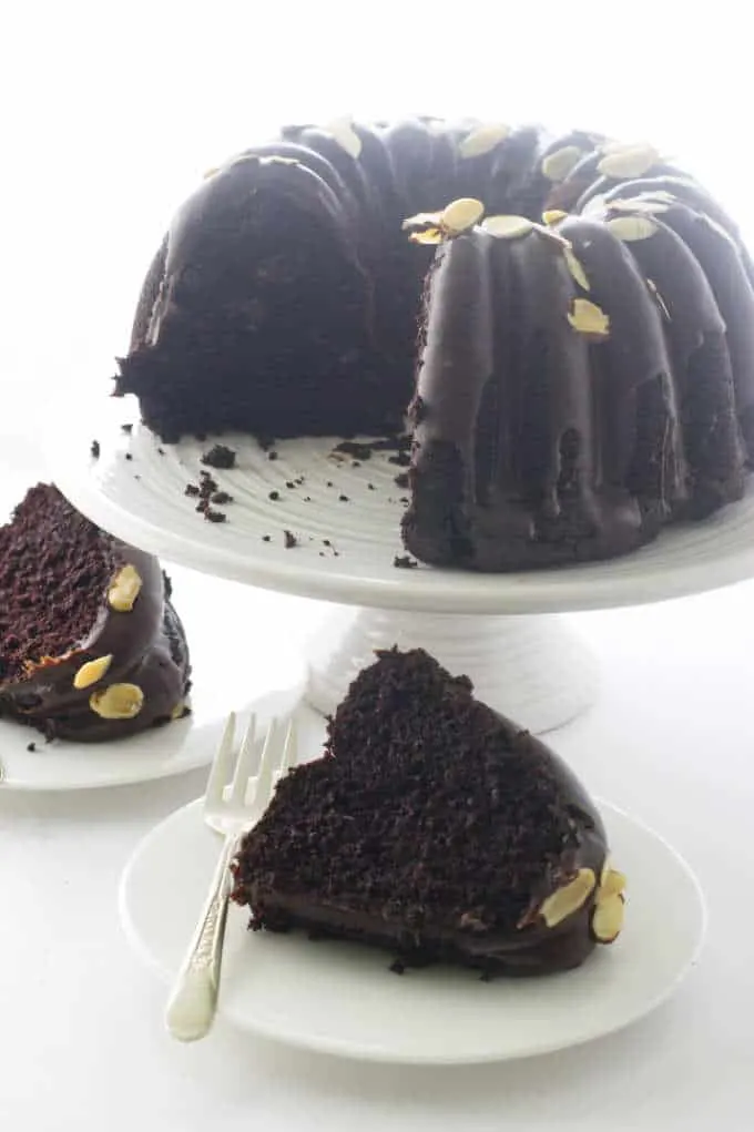 two slices of cake below a bundt cake on a stand
