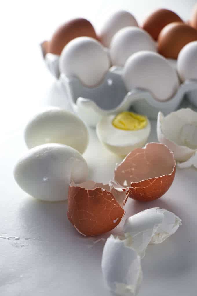 Brown and white egg shells with peeled hard boiled eggs in the background