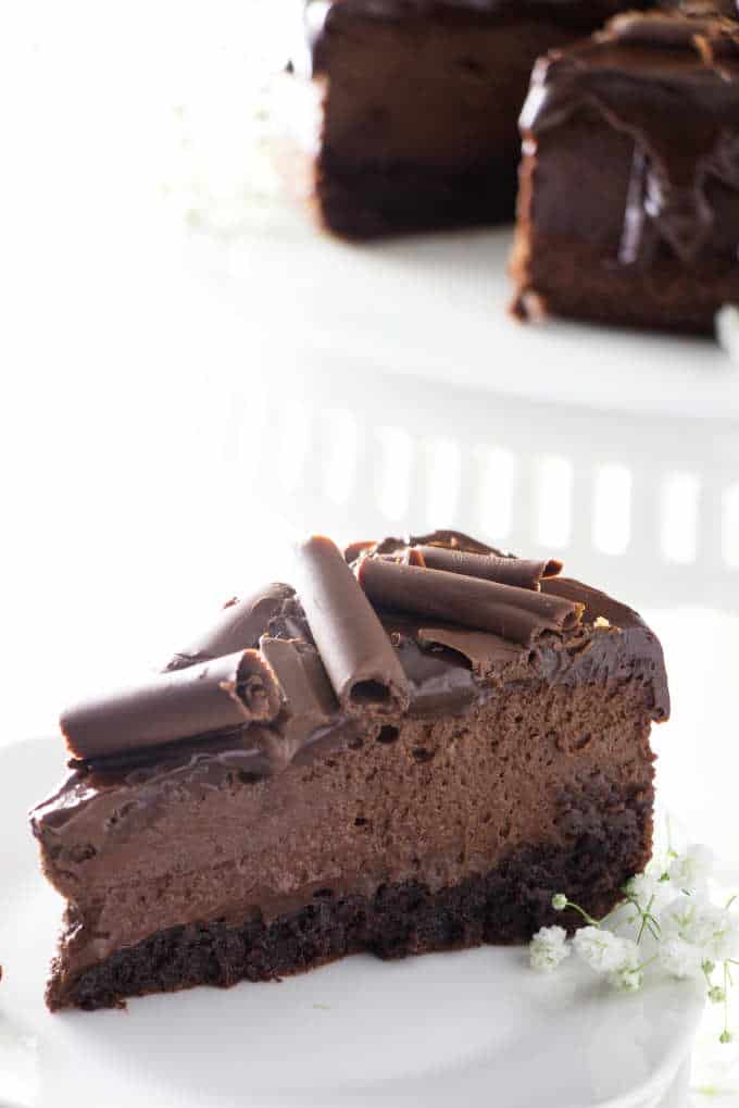 a slice of chocolate cheesecake with cake in the background