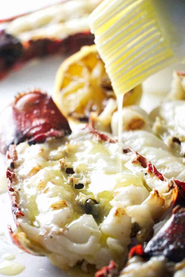 close up of a grilled lobster tail being drizzled with garlic butter sauce