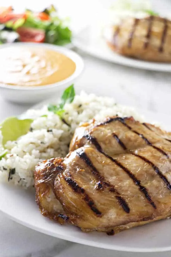 Two plates with grilled chicken breast and a bowl of spicy peanut sauce.