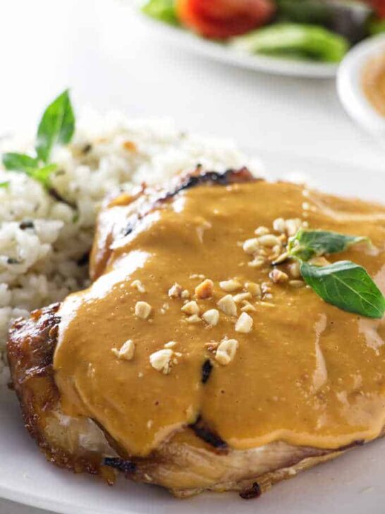 A grilled chicken breast topped with spicy peanut sauce plated with rice.