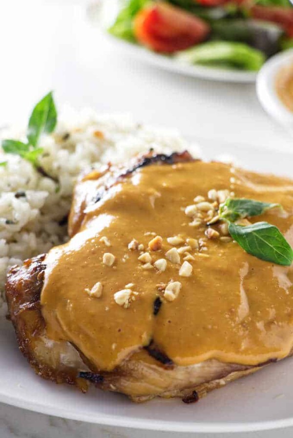 A grilled chicken breast topped with spicy peanut sauce plated with rice.