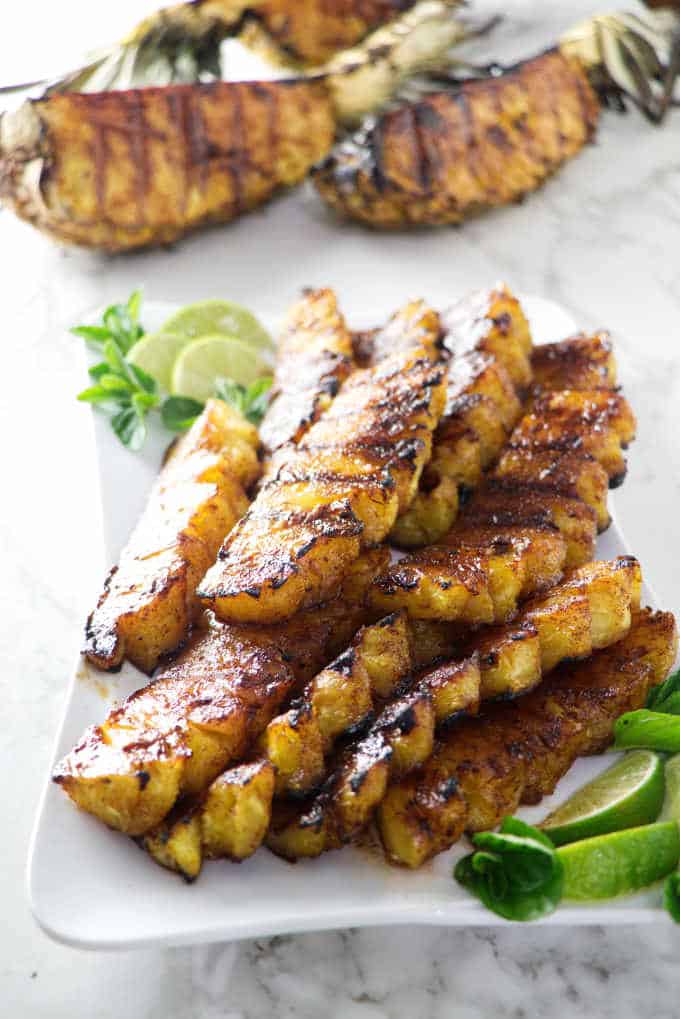 A plate of grilled pineapple spears with large quartered pineapples in the background. 