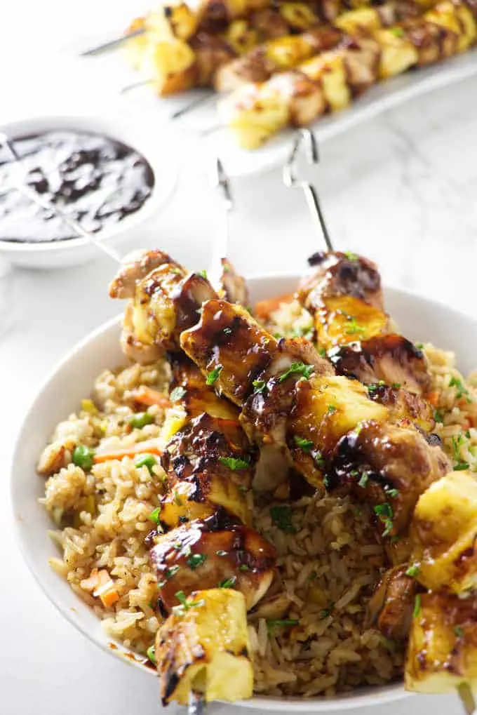 three pineapple chicken kabobs on a bowl of rice