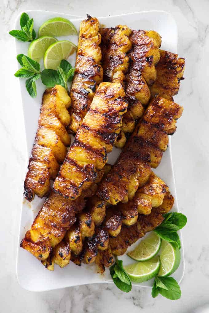 A plate of grilled pineapple garnished with limes and mint leaves