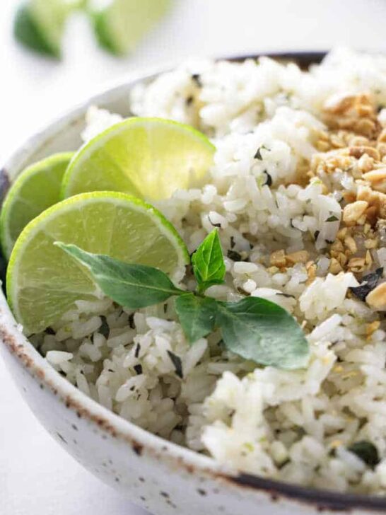 A bowl of basil lime rice with sliced limes in the background