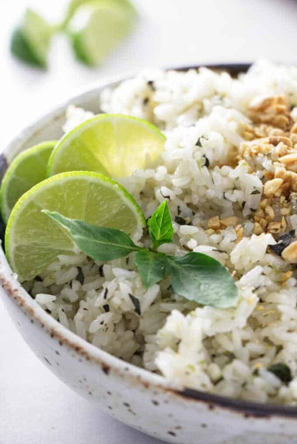 A bowl of basil lime rice with sliced limes in the background