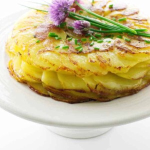 Crisp potatoes Anna on cake pedestal with fresh chive flowers