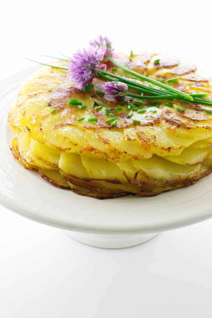 Crisp potatoes Anna on cake pedestal with fresh chive flowers