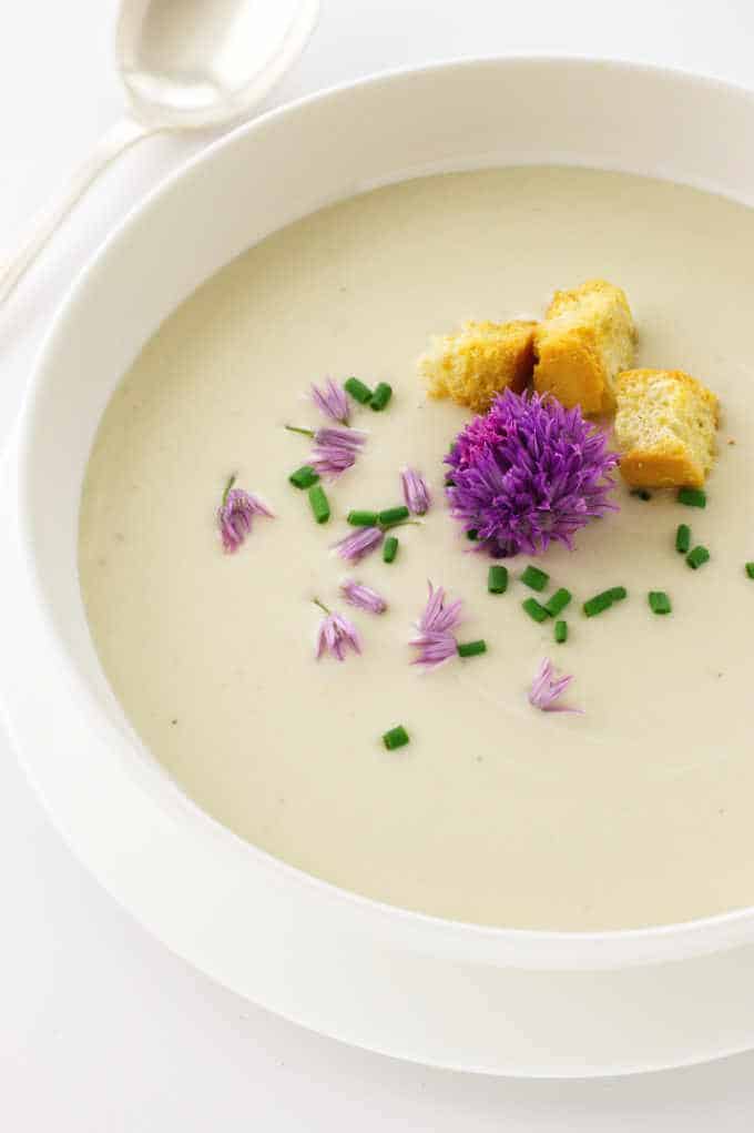 A bowl of soup garnished with chive blossoms, snipped chives and croutons.