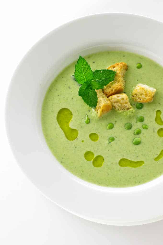 A close up serving of soup garnished with croutons, mint and finishing oil