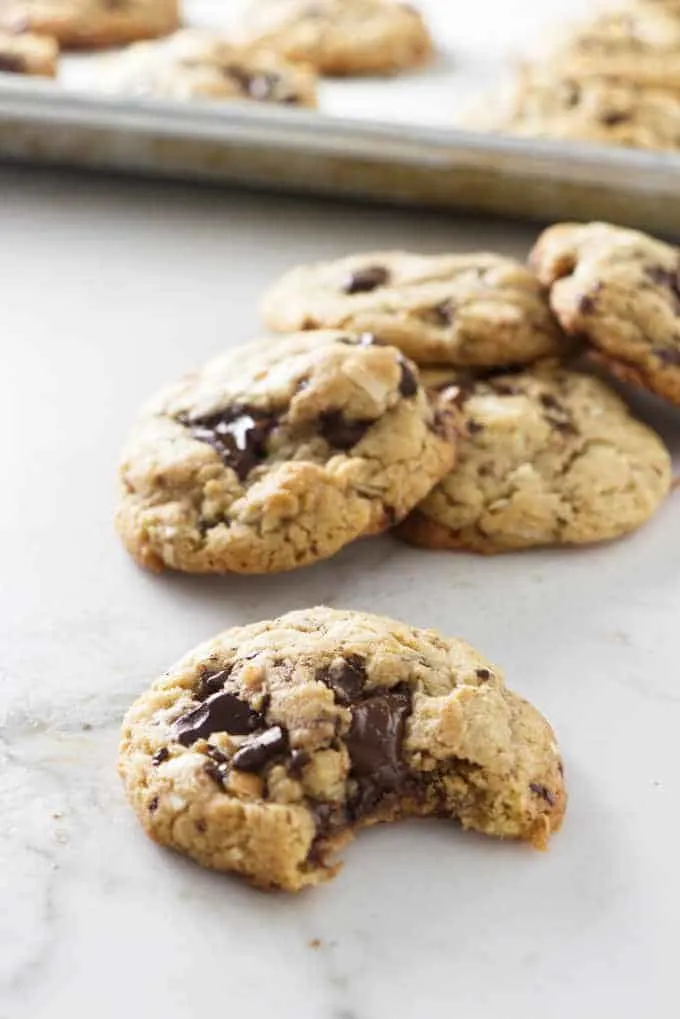 a pile of coconut chocolate chunk tahini cookies with a bite taken from one cookie
