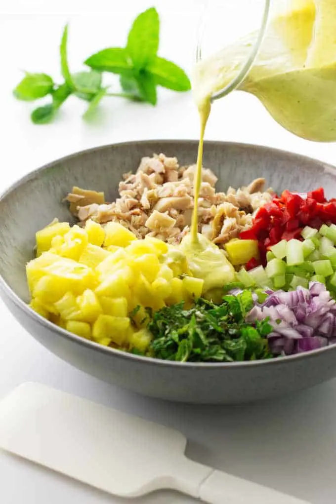 Salad bowl with pineapple-chicken mixture and curry dressing being poured on