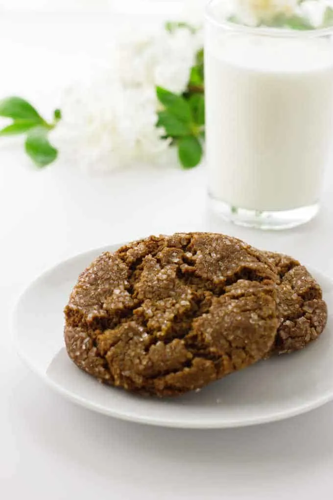 Two soft and chewy molasses spice cookies on a plate, glass of milk and flowers in background