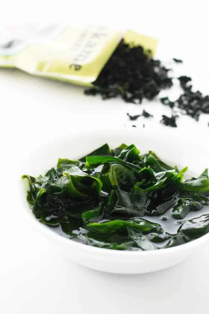 Wakame seaweed soaking in water with bag of dried wakame in background