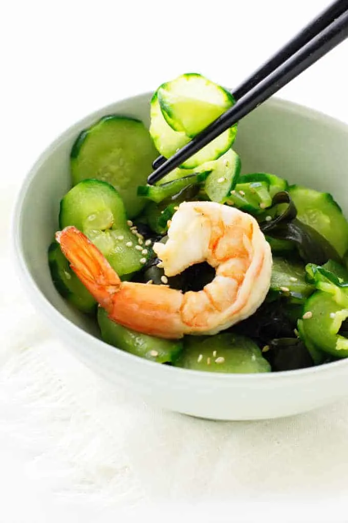 Chopsticks piking up slices of cucumber salad, boiled shrimp on top of salad