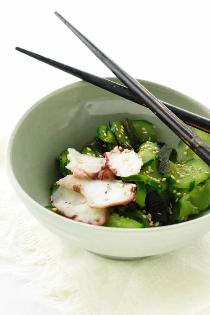 A dish of cucumber salad with sesame seeds and slices of cooked octopus