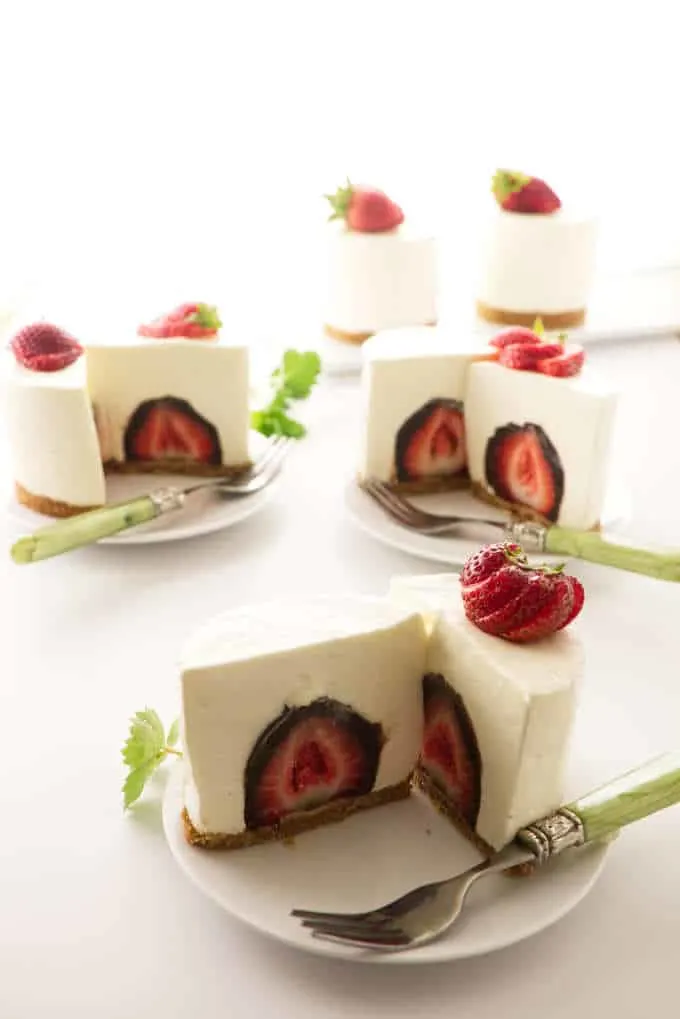 Three individual cheesecakes sliced open in the middle to see a chocolate covered strawberry
