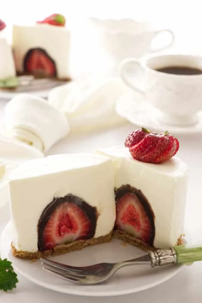 an individual cheesecake sliced open to reveal a chocolate covered strawberry. Coffee cup in the background. 