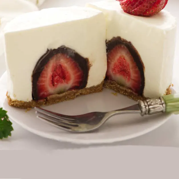 A small cheesecake sliced open to show a chocolate covered strawberry inside.