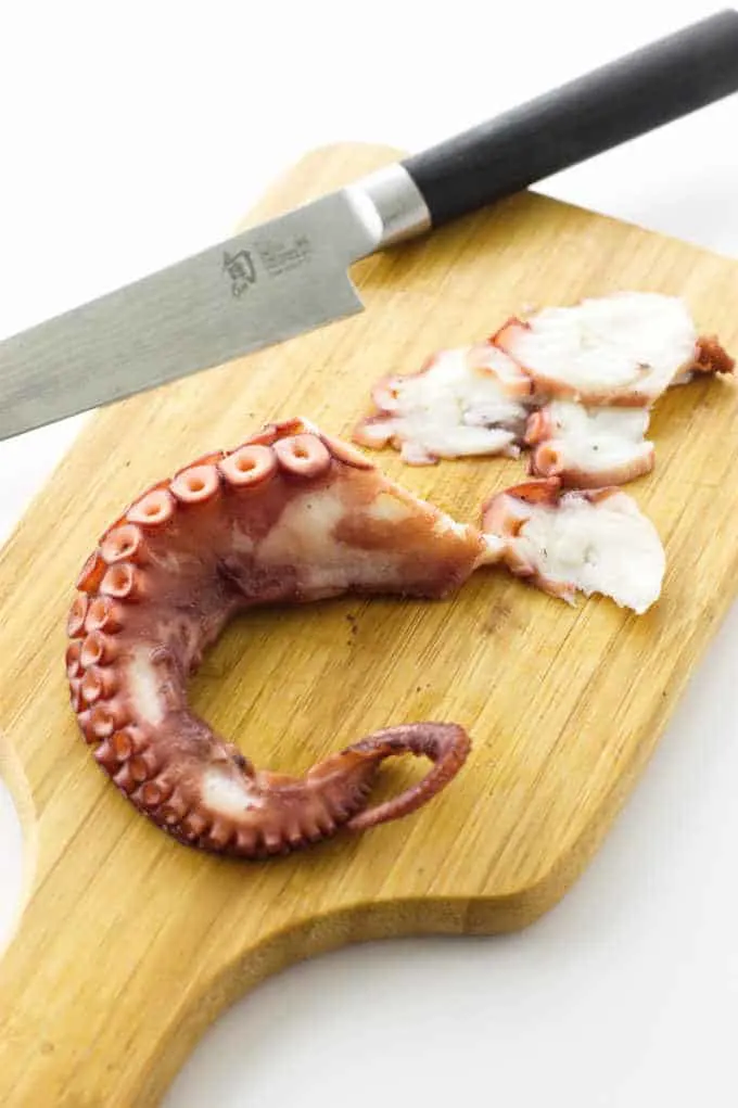Octopus leg with slices on cutting board with knife