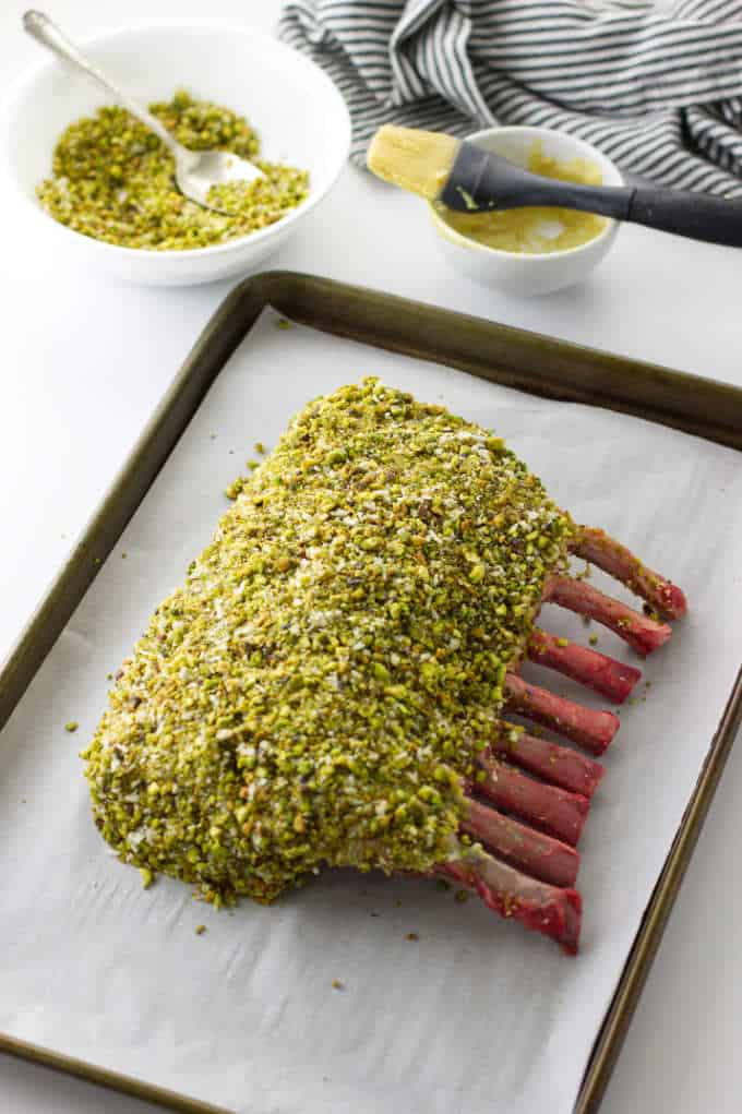 Overhead view of coated crust on rack of lamb, dish of mustard sauce and dish of crusting