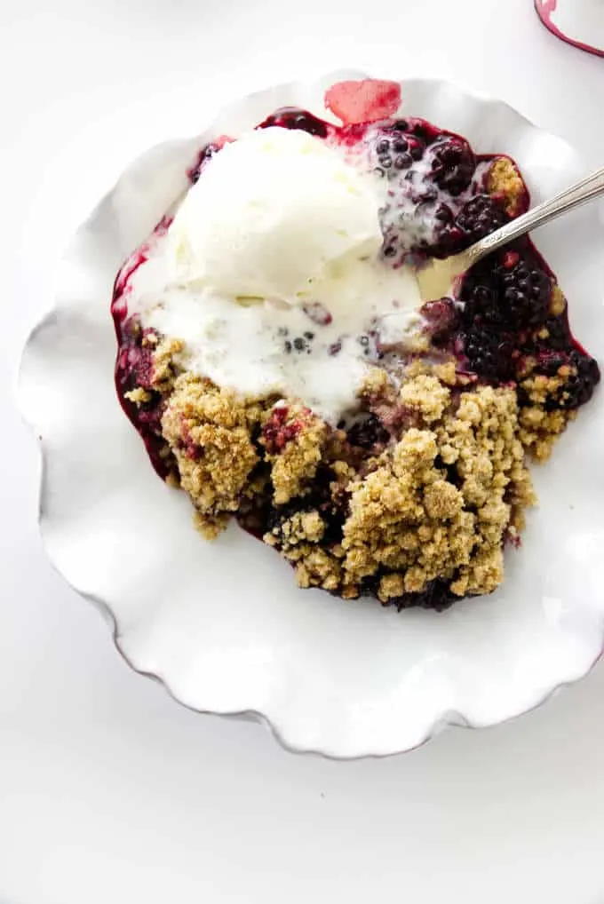 serving dish of blackberry crumble with vanilla ice cream