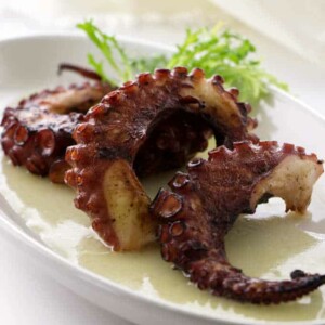 Three grilled octopus legs in pool of preserved lemon vinaigrette