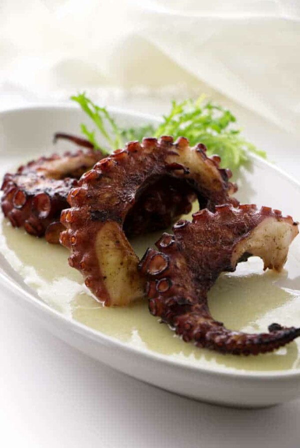 Three grilled octopus legs in pool of preserved lemon vinaigrette